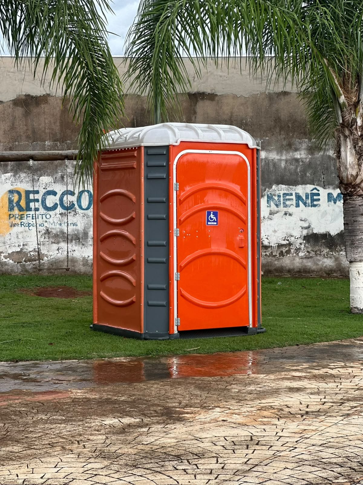 Banheiro PCD/PNE laranja com o símbolo de acessibilidade, montado no gramado de uma praça