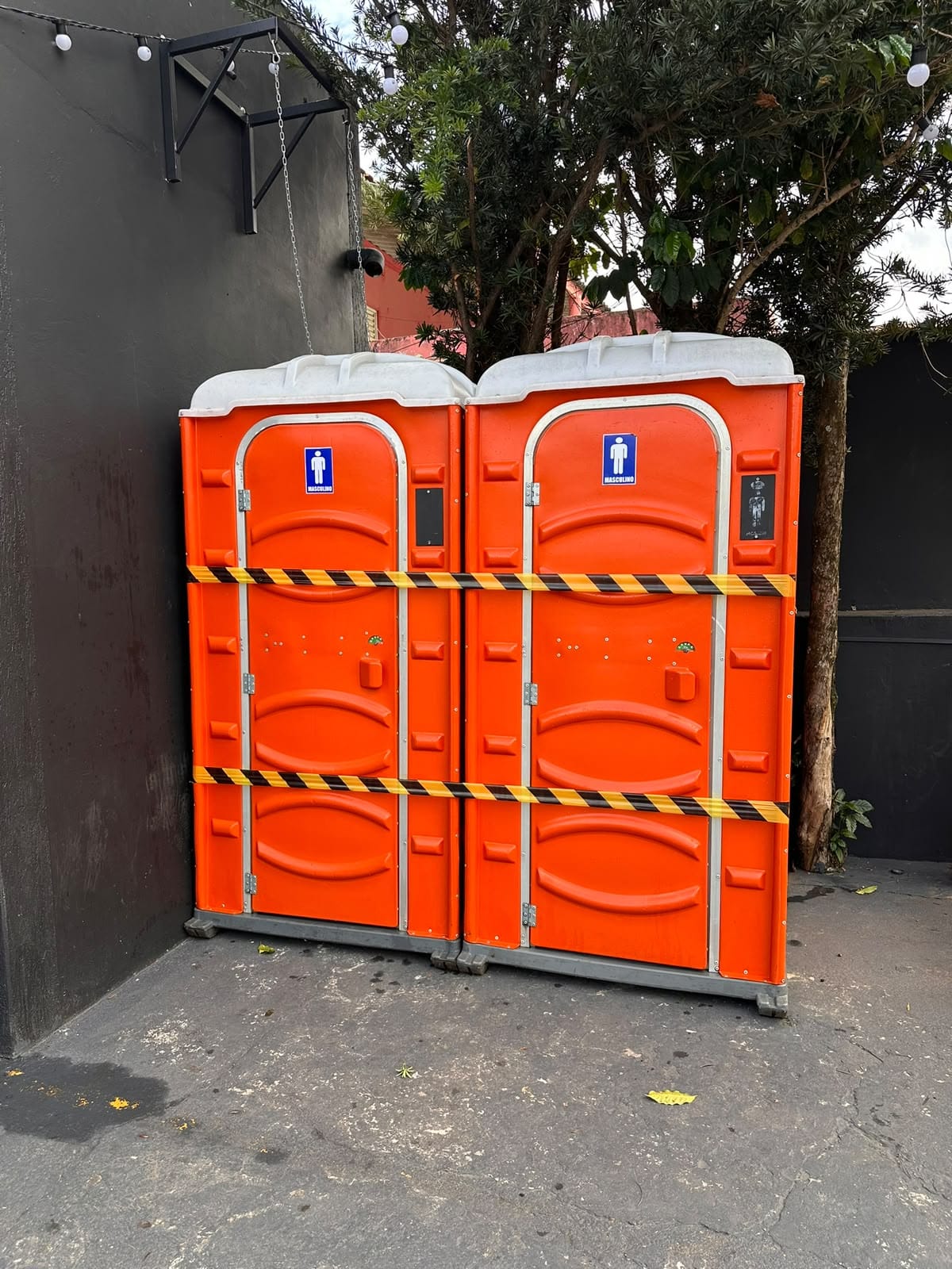 Dois banheiros químicos laranja lado a lado, isolados com fita