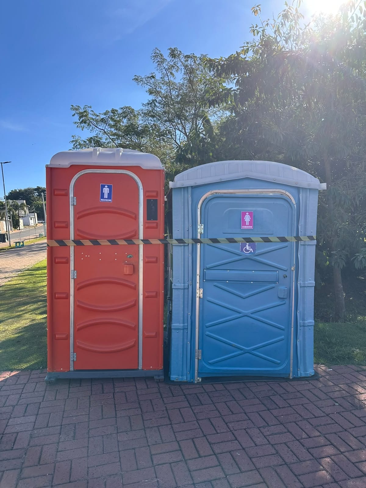 Banheiro STD laranja ao lado de um banheiro PCD/PNE azul-claro, em praça