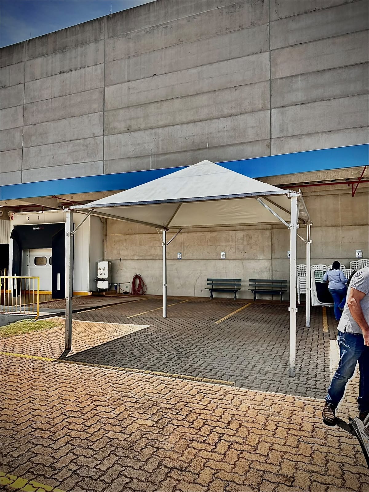 Tenda 5×5 branca montada sobre piso intertravado, ao lado de um galpão