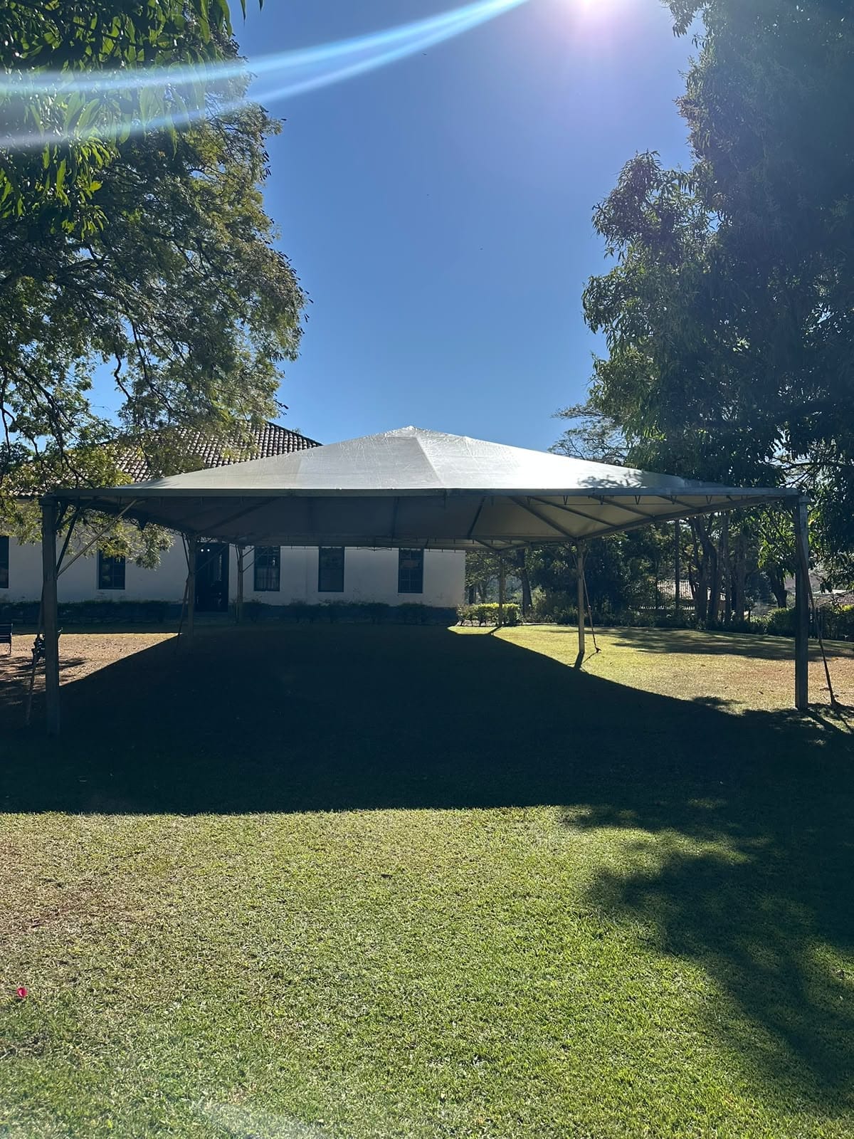 Tenda branca ampla montada no gramado de uma fazenda, com árvores ao redor