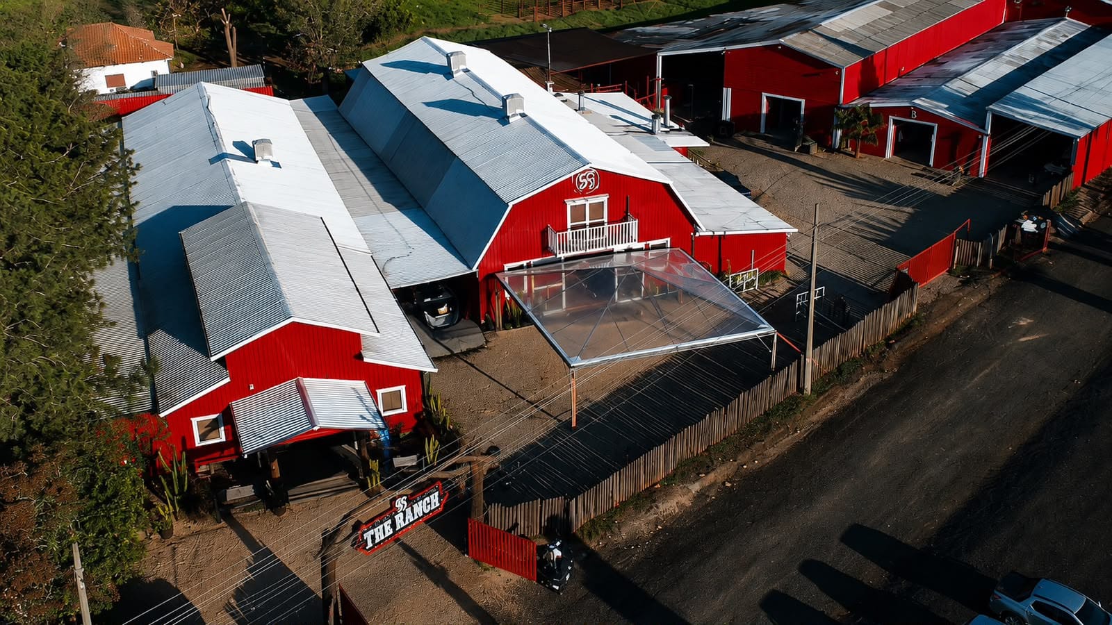 Vista aérea de um espaço com galpões vermelhos e a tenda montada em frente a um deles