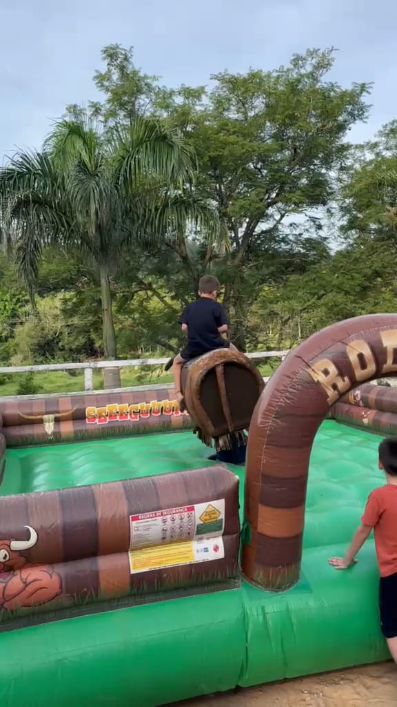 Criança no touro mecânico, ao lado do arco da arena inflável